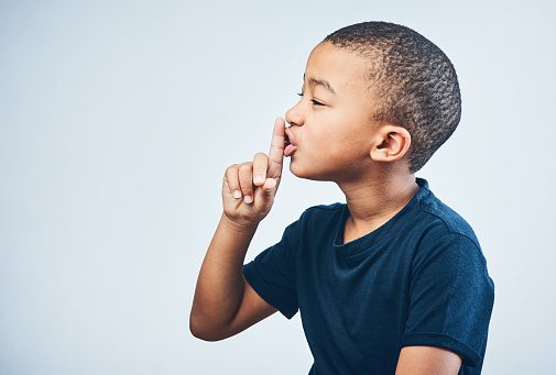 Studio shot of a cute little boy posing with his finger on his lips against a grey background