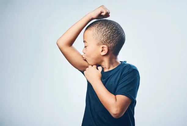Studio shot of a cute little boy kissing his muscles against a grey background
