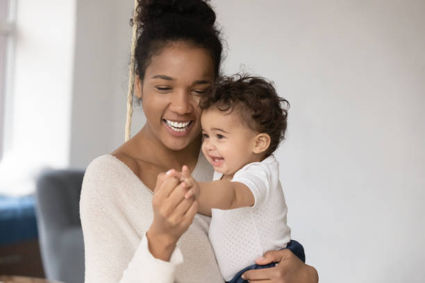 Happy young mixed race mother holding funny little infant kid on hands, enjoying playtime activity together indoors. Affectionate loving african ethnicity mum having fun with adorable small baby.