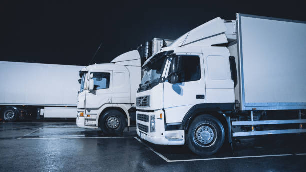 istock White Semi-Trucks with Cargo Trailer Standing on Overnight Parking Place. Drivers Resting at Night on the Overnight Parking Lot. 1271954939