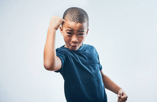Studio shot of a cute little boy flexing his muscles against a grey background