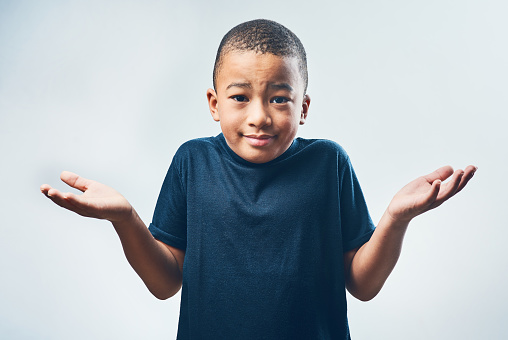 Studio shot of a cute little boy shrugging his shoulders against a grey background