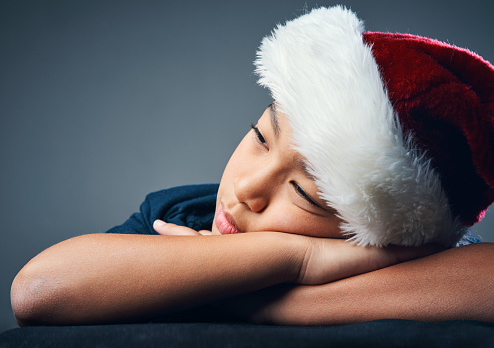 Studio shot of a cute little boy wearing a Santa hat and looking thoughtful against a grey background
