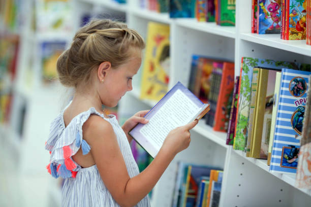 A little girl stands in a bookstore and reads. A little girl stands in a bookstore and reads. Child in the library. book bookstore sale shopping stock pictures, royalty-free photos & images