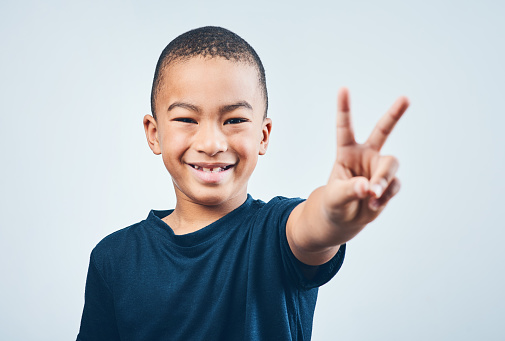 Studio shot of a cute little boy making a peace sign against a grey background