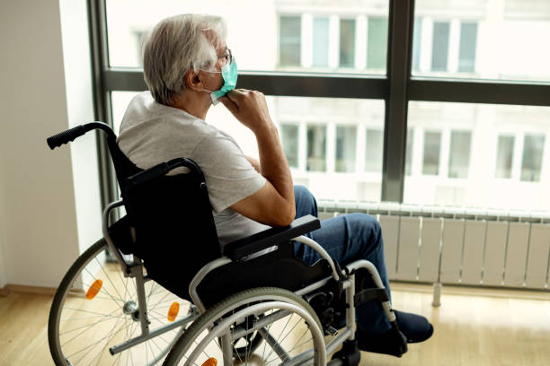 hombre de último año pensativo que usa máscara facial mientras está sentado en silla de ruedas y mirando a través de la ventana. - pensive senior adult looking through window indoors fotografías e imágenes de stock