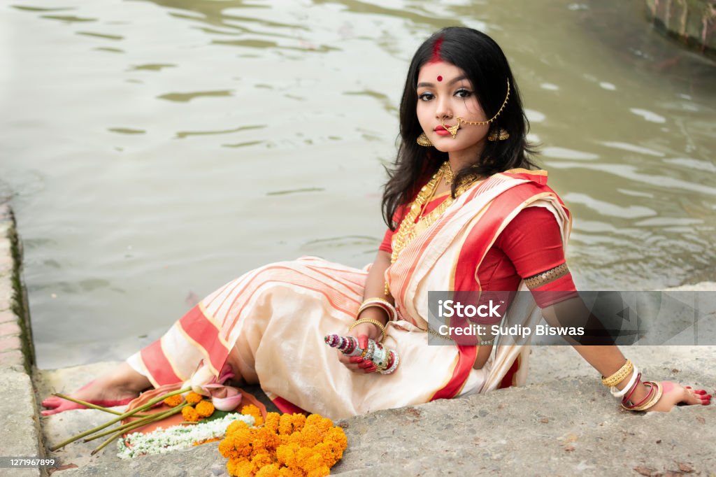 Portrait Of Beautiful Indian Girl In Front Of Ganga River Wearing Traditional Indian Saree Gold Jewellery And Bangles Holding Plate Of Religious Offering Maa Durga Agomoni Shoot Concept Stock Photo - Download Portrait Of Beautiful Indian Girl In Front Of Ganga River Wearing Traditional Indian Saree Gold Jewellery And Bangles Holding Plate Of Religious Offering Maa Durga Agomoni Shoot Concept Stock Photo - Download