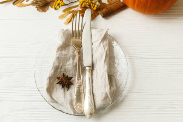 istock Stylish and zero waste Thanksgiving table setting. Plate with cutlery, linen napkin, anise and autumn leaves, pumpkin, autumnal flowers on white table. Rustic autumn wedding table set. 1271970763