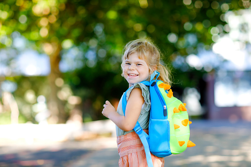 Cute little adorable toddler girl on her first day going to playschool. Healthy beautiful baby walking to nursery preschool and kindergarten. Happy child with backpack on the city street, outdoors