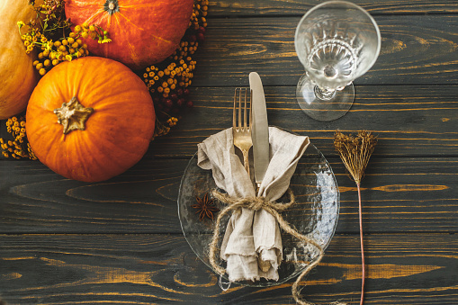 Eco friendly Thanksgiving dinner table setting. Stylish plate with cutlery, linen napkin with herb and pumpkin with autumn flowers on rustic table. Farmhouse rustic autumn wedding