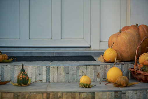 Cut out of the steps of the main entrance of a house that has been decorated with orange and yellow squashes and pumpkins for a traditional Halloween season.
