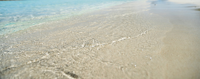 Sandy empty beach, ocean transparent rippled Aegean sea water touch wet sand close up. Greece summer vacation, Cyclades island. Space