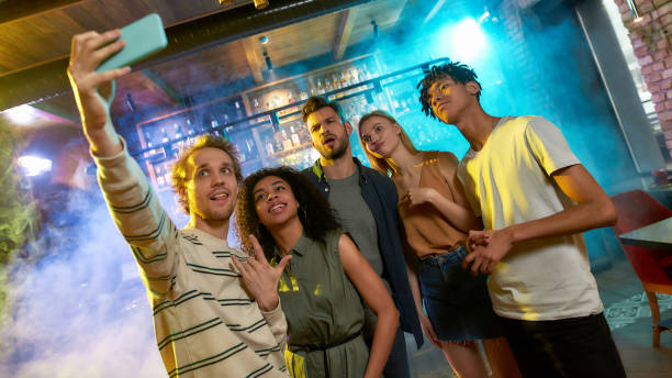 istock Selfie time. Young men and women smiling while taking selfie using smartphone. Multiracial group of friends hanging out at party in the bar 1271979269
