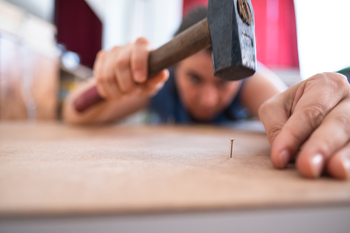 Young woman hammering a nail into wooden board