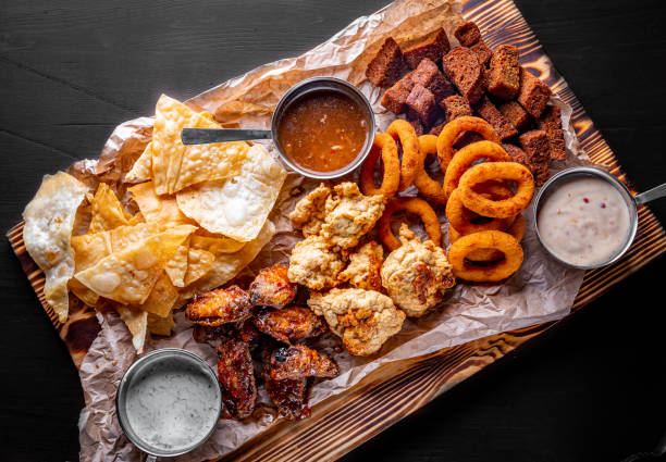 plato de cerveza con alitas de pollo picante, patatas fritas, aros de cebolla fritas, bolas de queso, empanado, salsa tártara en la mesa de madera - beer wing spicy chicken wings chicken wing fotografías e imágenes de stock