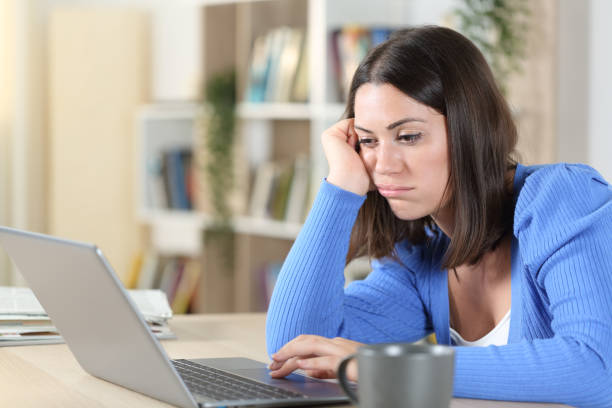 kuvapankkikuvat ja rojaltivapaat kuvat aiheesta tylsistynyt nainen tarkistaa kannettavan tietokoneen työpöydältä kotona - slow