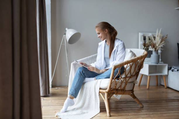 istock Attractive young woman using digital tablet and smiling while sitting in chair at home. 1271991751