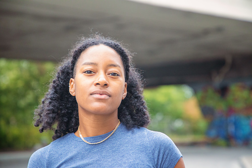 Confident strong female urban portrait below overpass. She is looking at the camera chin up, with a solid attitude.