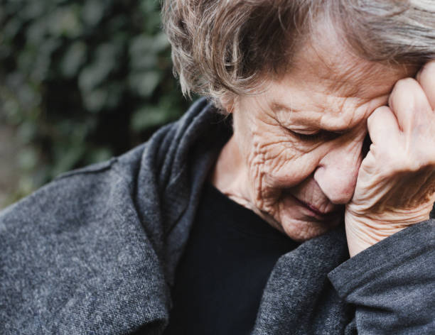 senior woman holds her head as she is stricken by grief - women guilt uncomfortable human face imagens e fotografias de stock