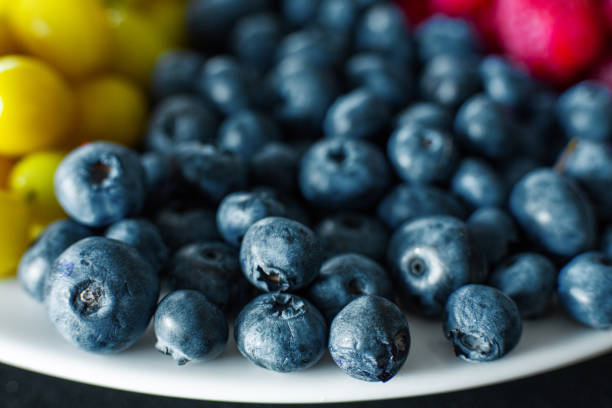 View from above. A mix of yellow, red and blue berries in a white grater. Triangle separation. Summer mix of fruits. Berry layout.