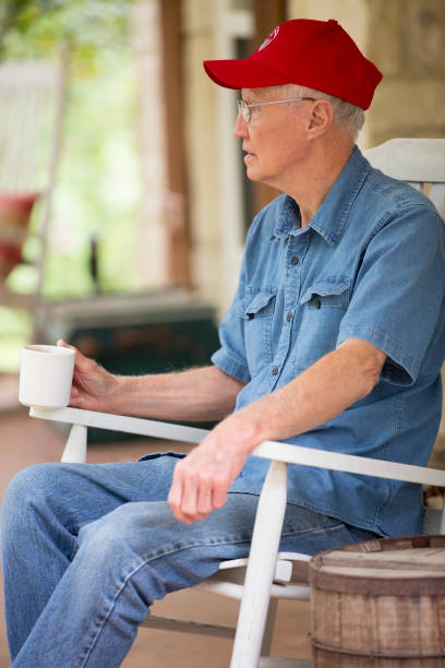 senior mann sitzt in rocker auf veranda genießen seinen kaffee - baseball cap old red caucasian stock-fotos und bilder