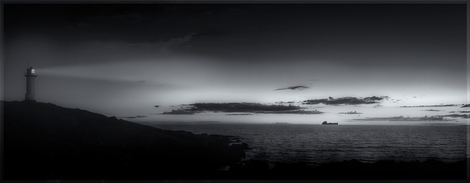 Panorama with dramatic light and sky with a beautiful old lighthouse in front, sunset, ship in background at the horizon