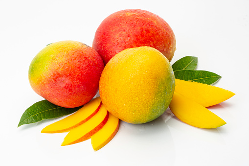 Three beautiful ripe mangoes, mango slices and mango tree leaves, studio shot.