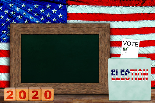 US elections concept with American flag hung behind wooden frame chalkboard for copy space, and ballot box with voter slip. Concept of presidential, senate and house of representatives elections in 2020.