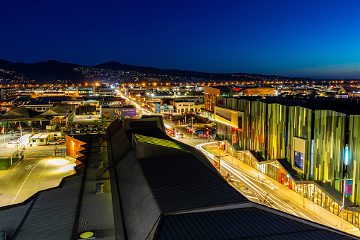 In this 11 September 2020 long-exposure photo shot at dusk, the mixed progress of the decade-long earthquake rebuild efforts in Christchurch Central are apparent. In the foreground centre is the Bus Interchange which opened in 2015. In the foreground right is the Christchurch EntX (Entertainment Central) building which features movie theatres and restaurants that opened in 2018. In the background are a number of car parks. Low-rise buildings damaged by the quakes used to occupy those sites. Empty spaces are a common sight across Christchurch where buildings once stood. The Port Hills are visible in the distance. The Canterbury Earthquakes struck on 4 September 2010 and 22 February 2011.