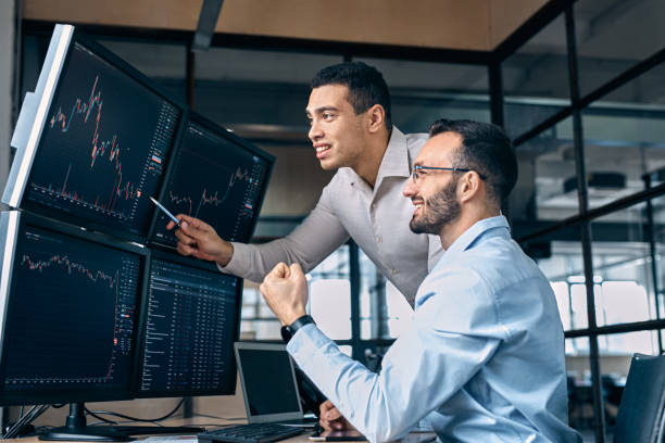 istock Teamwork Concept. Traders sitting at office together monitoring stocks data on screen analyzing price having profit smiling cheerful 1272017266