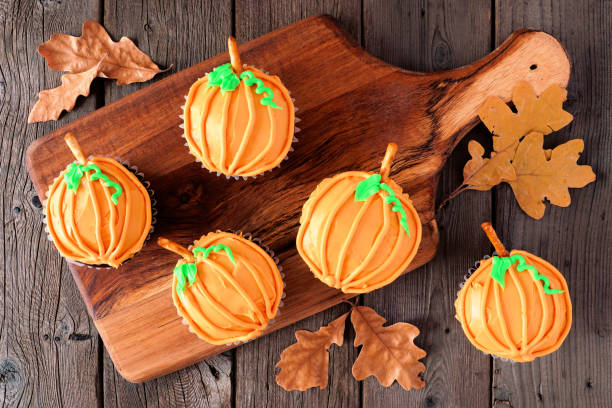 Autumn pumpkin cupcakes on a wooden serving platter over rustic wood Autumn pumpkin cupcakes on a wooden serving platter. Above view on a rustic wood background. halloween cupcake stock pictures, royalty-free photos & images