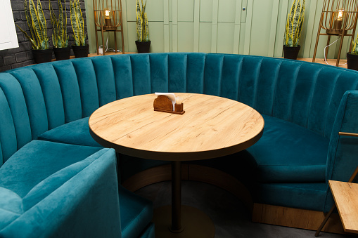 Large round sofa in blue for a large company around a round wooden table. Interior of a restaurant.