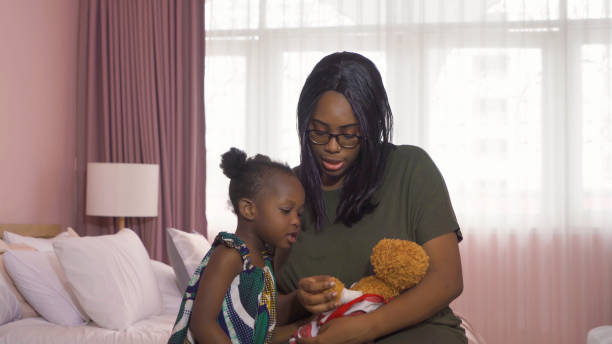 笑顔のビジネス黒人アフリカ系アメリカ人女性の肖像画、ピンクの背景に家族関係の概念でクマの人形のおもちゃを演じる彼女の娘とママ。彼女の親と黒い子供の幼児の女の子。 - family single mother black mother ストックフォトと画像