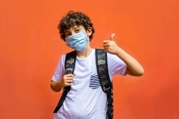 Schoolchild wearing a covid-19 surgical mask thumbs up. Back to school at new normal after coronavirus quarantene lockdown concept. schoolboy stock pictures, royalty-free photos & images