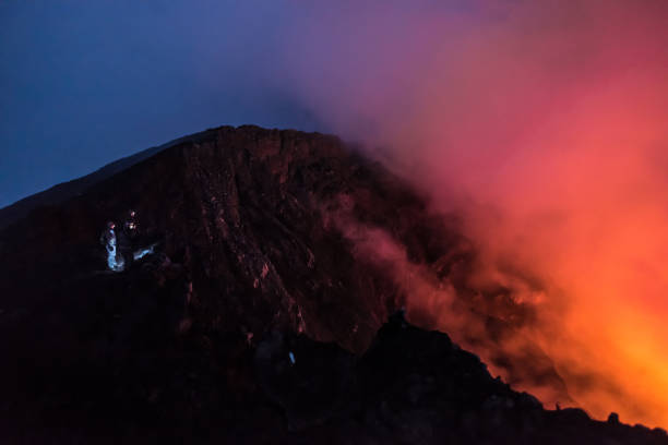 un groupe de personnes se tiennent au bord de cratère du volcan actif de nyiragongo rempli de fumée au lever du soleil - lava lake photos et images de collection