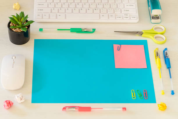 a large, blank blue card on the desk and a small pink card with space for text. office and school accessories, computer keyboard, pens, crumpled paper balls, scissors, mini flower in a pot, staples. concept - binary code close up computer data imagens e fotografias de stock