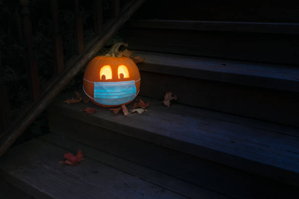 illuminato halloween jack o lantern zucca indossando maschera covid ppe sui gradini di notte - low key lighting foto e immagini stock