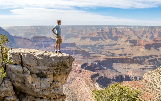 Young man standing on rocky ledge, staring out over the Grand Canyon - Grand Canyon National Park, Arizona, USA