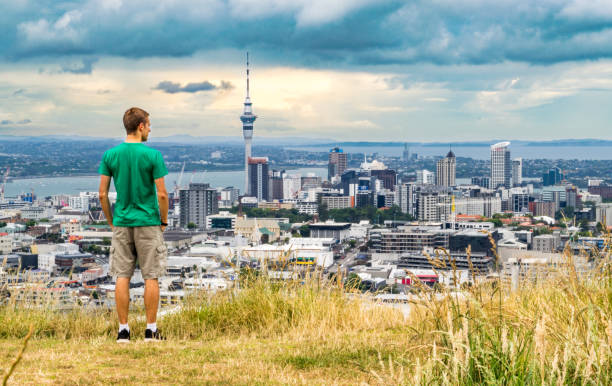 Young Explorer Gazing at Auckland Skyline from Hill Young man standing on the summit of Mt. Eden overlooking the Auckland skyline at sunset - Auckland, New Zealand (city center/ downtown) auckland stock pictures, royalty-free photos & images
