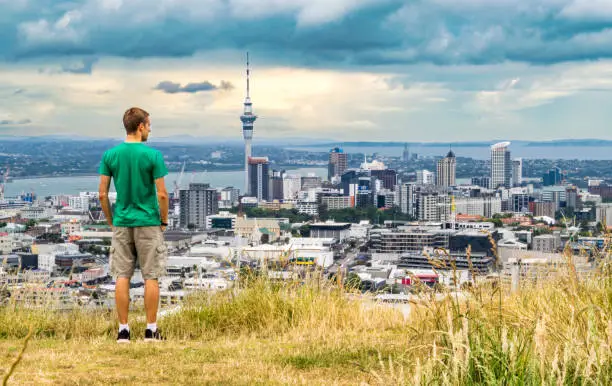 Young man standing on the summit of Mt. Eden overlooking the Auckland skyline at sunset - Auckland, New Zealand (city center/ downtown)
