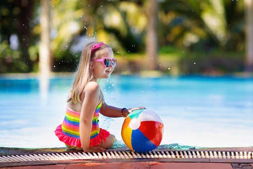 Child in swimming pool with inflatable toy ball. Kids swim. Colorful rainbow float for young kids. Little girl having fun on family summer vacation in tropical resort. Beach and water fun.