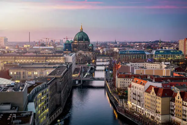 View along the river Spree to the Berlin Cathedral and  urban skyline of Berlin, Germany, with city lights and soft sunset sky