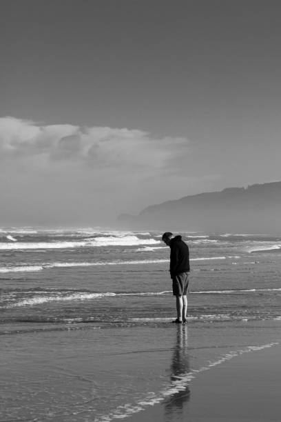 istock Man looking down standing in front of the ocean in black and white 1272085790