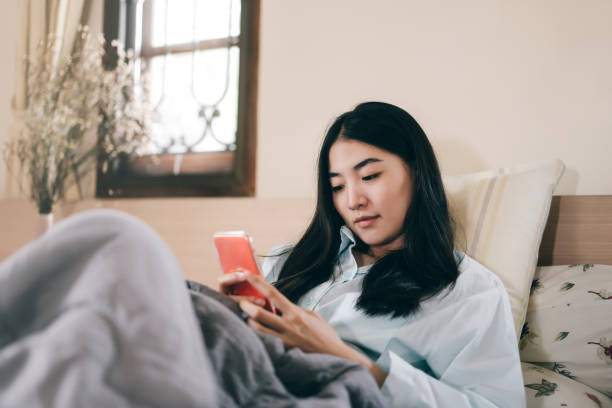 joven adulto solitario mujer soltera usando computadora portátil en la mañana para el chat de la aplicación de mensajes sociales con amigo para la salud mental - working bed smart phone bedroom fotografías e imágenes de stock