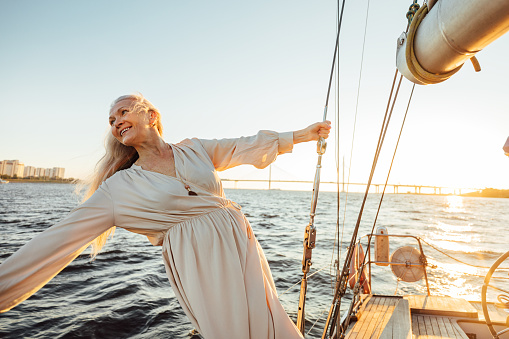 Mujer mayor alegre en vestido largo disfrutando de vacaciones en velero privado photo
