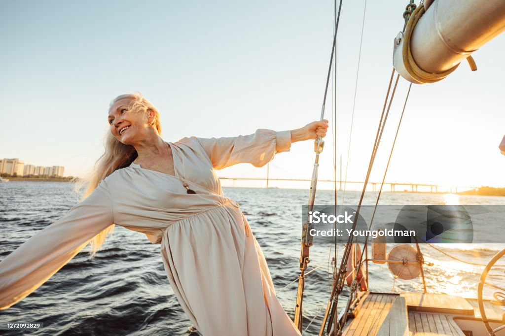 Cheerful senior woman in long dress enjoying vacation on private sailboat Long Dress Stock Photo