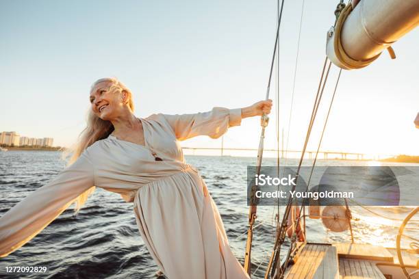 Cheerful Senior Woman In Long Dress Enjoying Vacation On Private Sailboat Stock Photo - Download Image Now