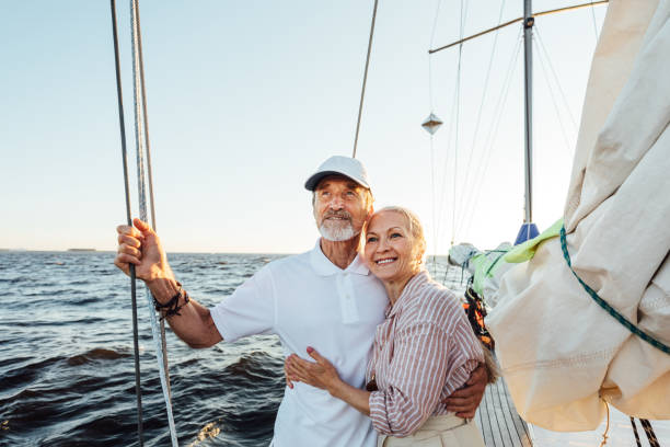 Loving senior couple enjoying vacation and looking to the distance. Mature couple standing together and embracing on a private sailboat. Loving senior couple enjoying vacation and looking to the distance. Mature couple standing together and embracing on a private sailboat. old boat stock pictures, royalty-free photos & images