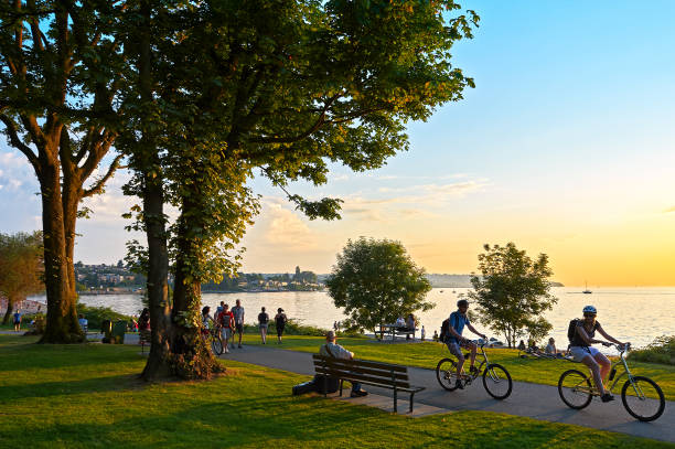 Young people biking, walking at Stanley Park Young couple cycling, others walking or jogging late afternoon and enjoying the sunset at Stanley Park Vancouver, British Columbia, Canada promenade stock pictures, royalty-free photos & images