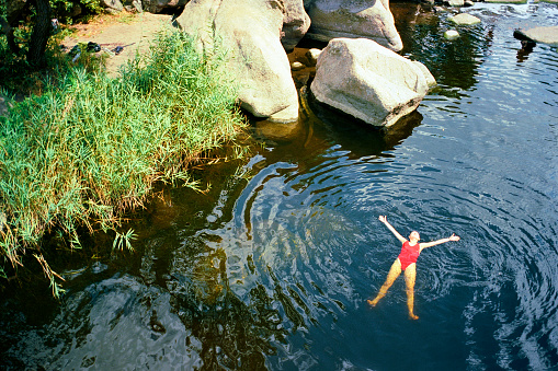 Young Caucasian woman swimming in river in summer. Camera film